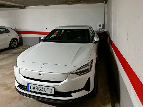 Coche eléctrico blanco estacionado en un garaje con paredes blancas y rayas rojas.