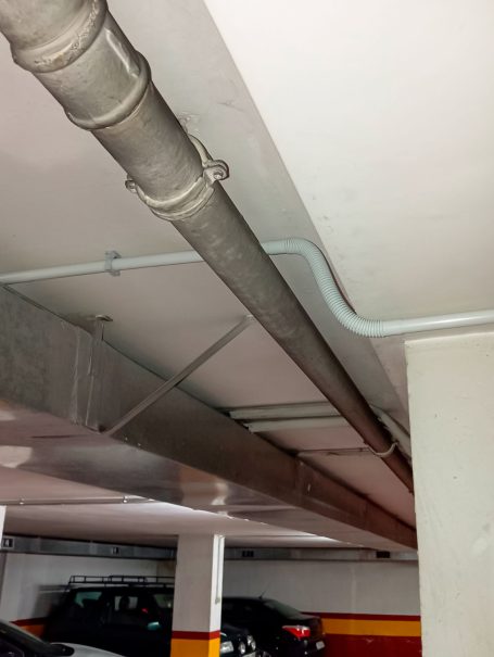 Tuberías metálicas y de PVC en un aparcamiento, sobre un fondo de paredes blancas y rojas.